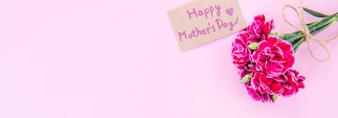 May mothers day idea concept photography - Beautiful blooming carnations tied by bow with kraft text card isolated on bright modern table, copy space, flat lay, top view