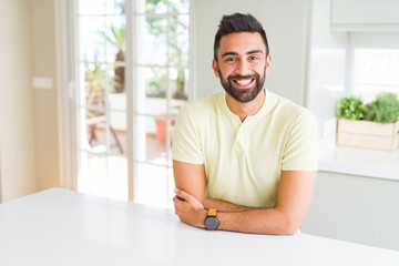 Handsome hispanic man casual yellow t-shirt at home happy face smiling with crossed arms looking at the camera. Positive person.