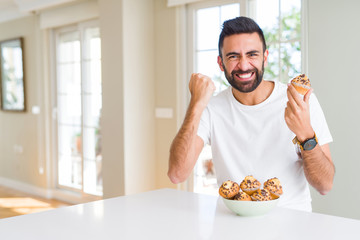 Handsome hispanic man eating chocolate chips muffin annoyed and frustrated shouting with anger, crazy and yelling with raised hand, anger concept