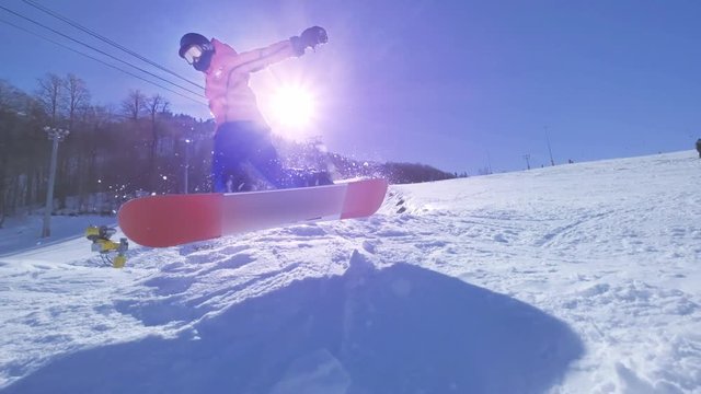 SLOW MOTION: Young pro snowboarder riding the half pipe in big mountain snow park, spraying snow into camera on halfpipe wall in sunny winter. Extreme snowboarder snowboarding and doing tricks.