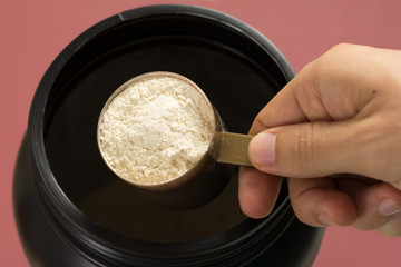 Whey Protein. Point of view of hand holding measuring scoop.  Vanilla flavour. Color background: brown.
