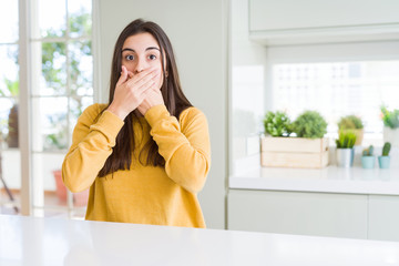 Beautiful young woman wearing yellow sweater shocked covering mouth with hands for mistake. Secret concept.