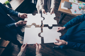 Cropped top above high angle view of stylish elegant sharks holding in hands fitting big large puzzle pieces together team building in loft industrial interior work place station