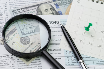 Magnifying glass with pen and calendar, 1040 US individual income tax filling form, tax submission or revenue calculation concept