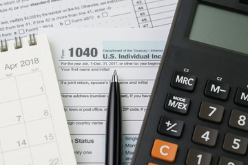 Calculator on calendar, pen and 1040 US individual income tax filling form, tax submission or revenue calculation concept