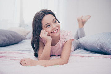 Obraz na płótnie Canvas Close up photo cute beautiful she her little girl crossed legs lying down hands arms hold head look side homey sunday wear home t-shirt pants comfortable bright light colored room inside indoors