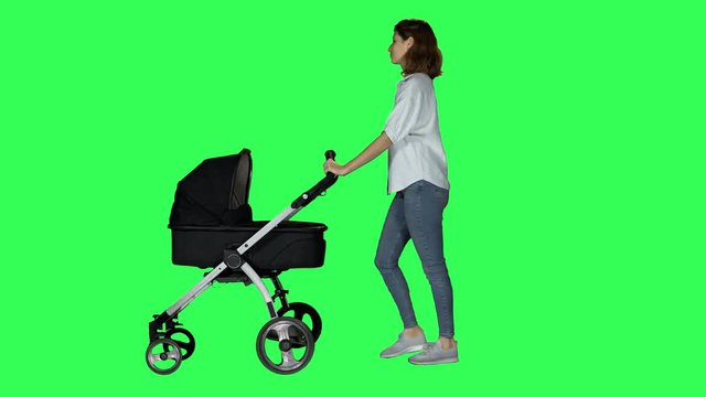 Casual mother waving hello while walking with a stroller, looking around and at her baby, smiling, over a green screen.