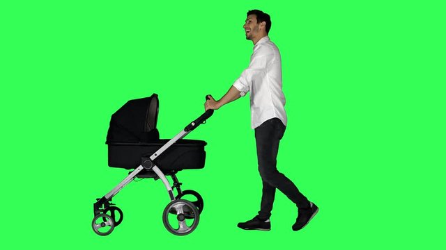 A dad walking with a stroller, looking around and at his baby, smiling, over a green screen.