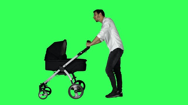 Happy father walking with a stroller, looking around and at his baby, smiling, over a green screen.