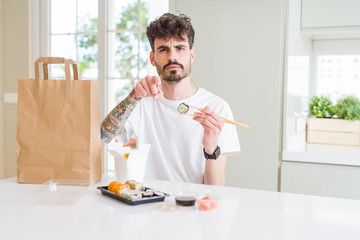 Young man eating asian sushi from home delivery pointing with finger to the camera and to you, hand sign, positive and confident gesture from the front