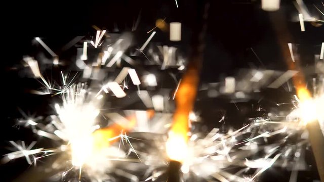 Close-up of sparkling sparklers in dark. Little festive fire fireworks on sticks are brightly shinning in darkness. Holiday element