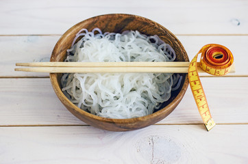 Chinese dietary noodles shirataki konjak in a wooden bowl with chinese chopsticks. Near the tape to measure the body. Gluten-free diet for weight loss.