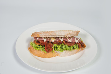 salami sandwich with lettuce, tomatoes and vegetable on white plate