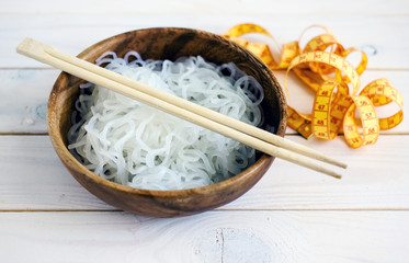 Chinese dietary noodles shirataki konjak in a wooden bowl with chinese chopsticks. Near the tape to measure the body. Gluten-free diet for weight loss.