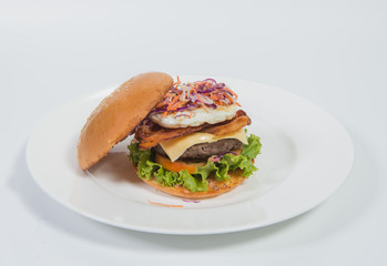 A delicious beef burger  with lettuce ,bacon ,cheese and topped with a fried egg on white