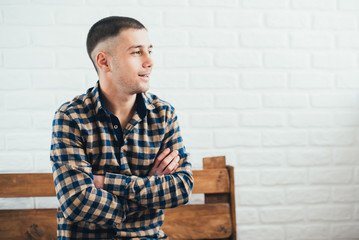 young guy sitting on a wooden bench of flying against a brick white wall