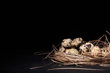 Quail eggs stacked in a pile or pyramid in a nest on a black background. Free space for input the text. Mockup for the Easter holiday. Matt effect