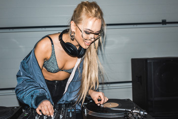happy blonde dj woman standing near dj mixer and vinyl record