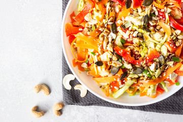 Asian coleslaw salad with white cabbage, carrot, pepper, sesame and cashew nuts. Healthy food concept. Light concrete background. Copy space.