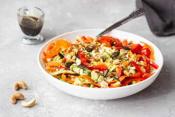 Asian coleslaw salad with white cabbage, carrot, pepper, sesame and cashew nuts. Healthy food concept. Light concrete background. Copy space.