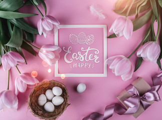 Easter eggs in nest and tulips flowers on pink background with Easter card. Waiting for spring. Top view with copy space