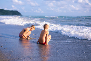Boy and girl playing on the beach on summer holidays. Children in nature with beautiful sea, sand and blue sky. Happy kids on vacations at seaside running in the water