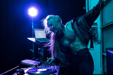 beautiful blonde dj girl touching dj mixer while standing in nightclub