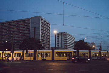 Vue du tramway jaune de Berlin dans son paysage urbain, au milieu du trafic et des immeubles. Des c&acirc;bles partout au dessus de la route.