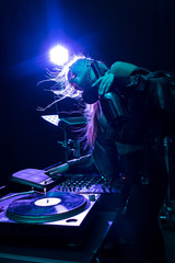 Happy blonde and stylish DJ girl touching DJ equipment in nightclub
