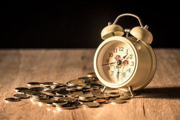 Clock and coins on wooden table, Money and time theme.