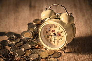 Clock and coins on wooden table, Money and time theme.