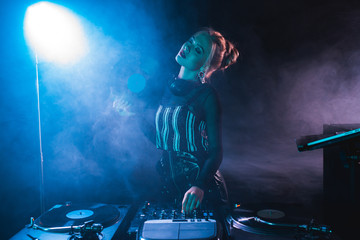 blonde dj woman standing with closed eyes near dj equipment and holding retro vinyl record in...