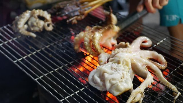 Cooking on grilling octopus at outdoor street asian market at night. Barbecue sea food. 4k