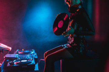cropped view of smiling dj woman holding retro vinyl record in nightclub with smoke