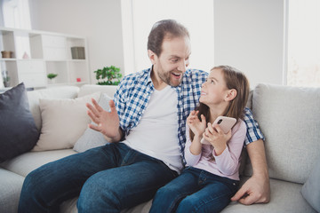 Portrait of his he her she nice lovely attractive pre-teen cheerful cheery amazed positive girl handsome bearded daddy sitting on divan talking speaking in light white interior room indoors