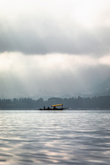 The beauty of Dal lake and the beautiful Shikaras in this minimal frame during the sunrise while the sun rays are peeking through the clouds