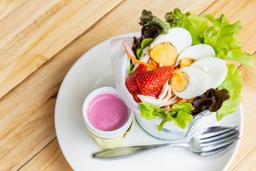 Close up fresh salad with boiled chicken and strawberry on bucket bowl on wooden table.