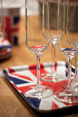 Empty clear Champagne Flute glases on a Union Jack British Flag tray standing on a wooden table.  In the background can be seen other partyware ready for use in a celebration.