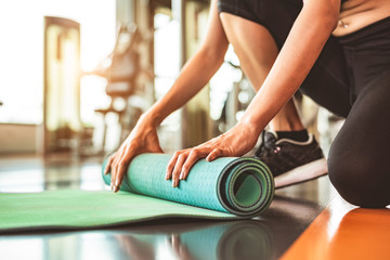 Close up of sporty woman folding yoga mattress in sport fitness gym training center background....
