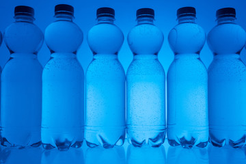 toned image of plastic water bottles in row on neon blue background with backlit