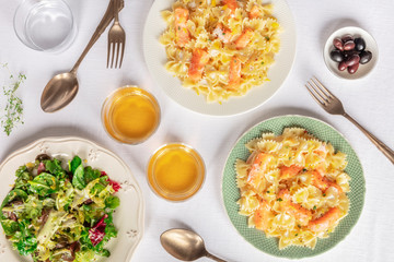 Two plates of salmon pasta. Farfalle with smoked salmon and cream sauce, shot from the top with wine and mesclun salad leaves