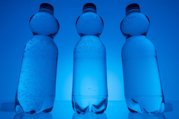 toned image of transparent plastic bottles with water on neon blue background