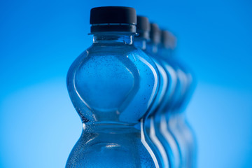 close up of transparent plastic water bottles with bubbles in row on blue background