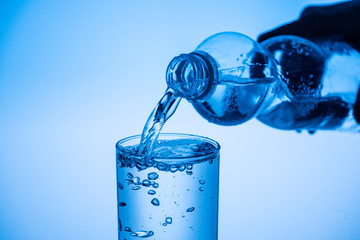 partial view of man pouring water from plastic bottle in glass on blue background