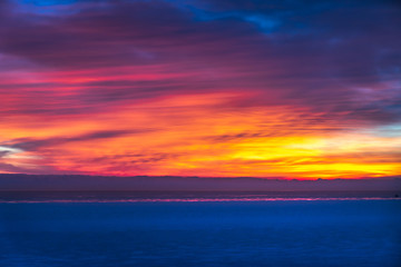 Gorgeous dramatic closeup sunrise photograph of the blue waters of Lake Michigan with orange, yellow, pink, purple and blue clouds in the sky above making a beautiful background.
