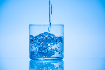 toned image of water pouring in drinking glass on blue backdrop with copy space