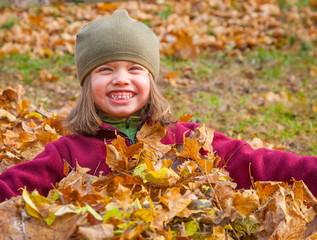 Smiling Little Girl Setting In Fall Leaves
