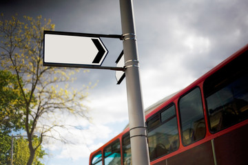 Blank street treet sign on a lamppost with a tree to the left and red bus to the right.