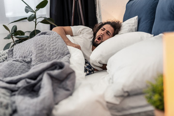Obraz na płótnie Canvas Sleepy young man yawning in the bed