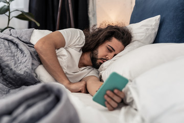 Sleepy brunette man looking at his smartphone screen